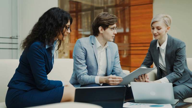 Diverse group of finance and sales professionals collaborating at a whiteboard filled with workflow diagrams, KPIs, and closing milestone markers
